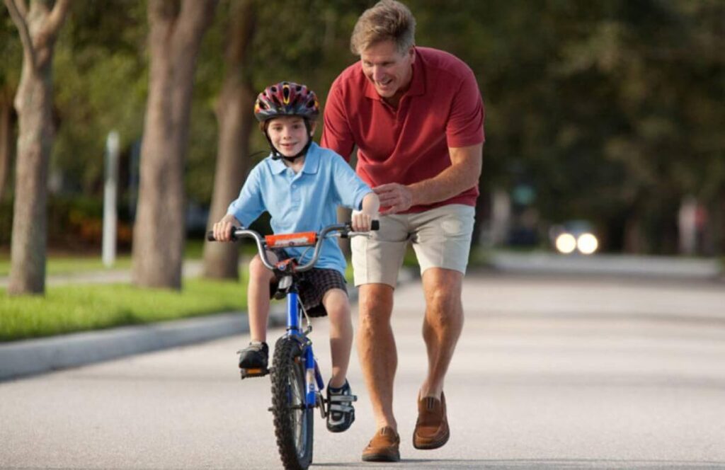 Pai segurando a bicicleta para o filho pedalar- seguro mais barato