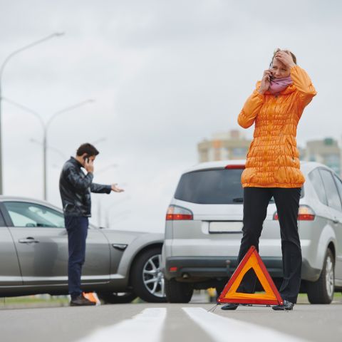 Dois motoristas ao telefone após colisão entre veículos em via urbana.